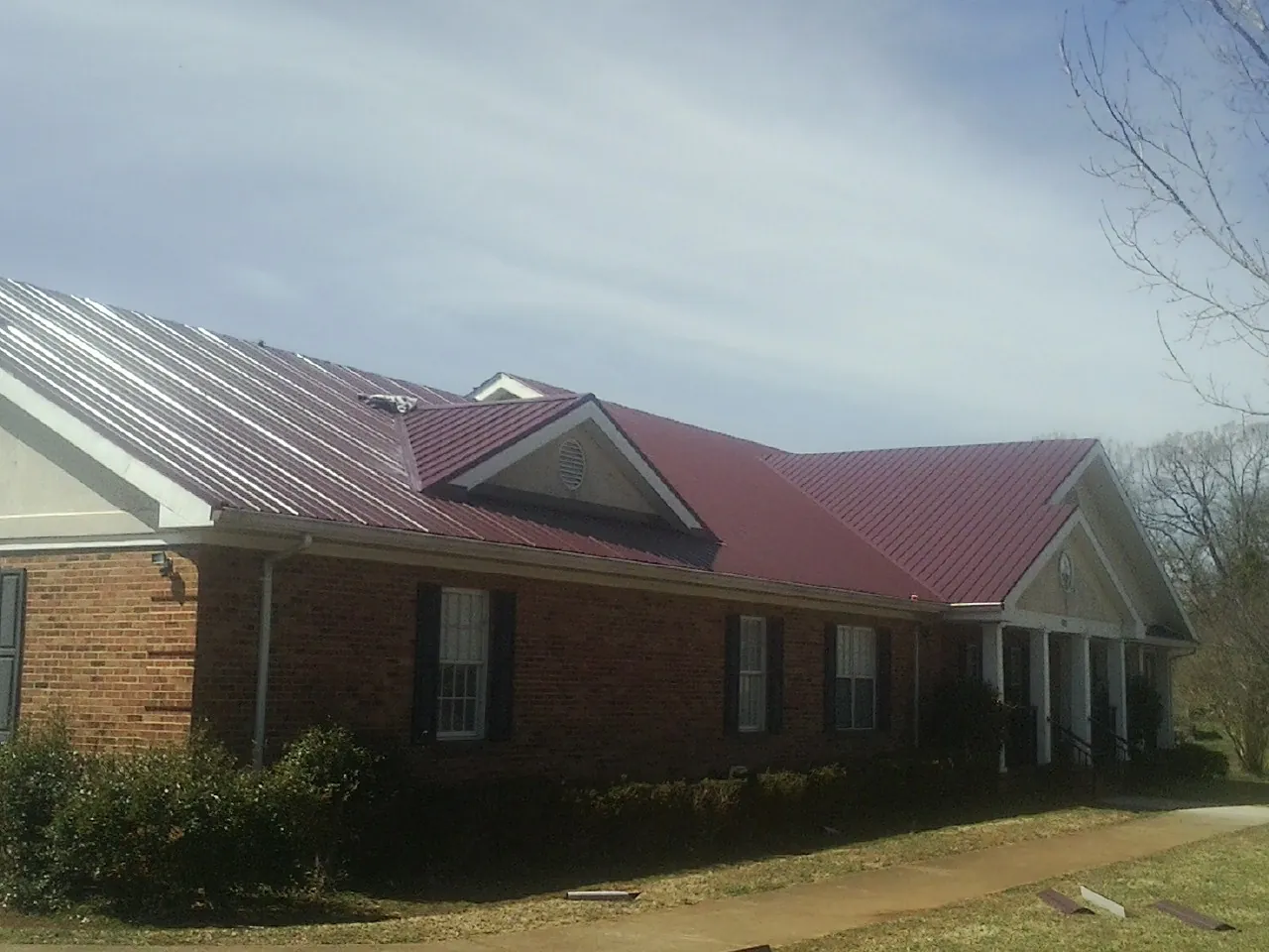 Red metal roof with gabled entries on a long brick building, from a Hail Damage Roof Repair job in Flower Mound