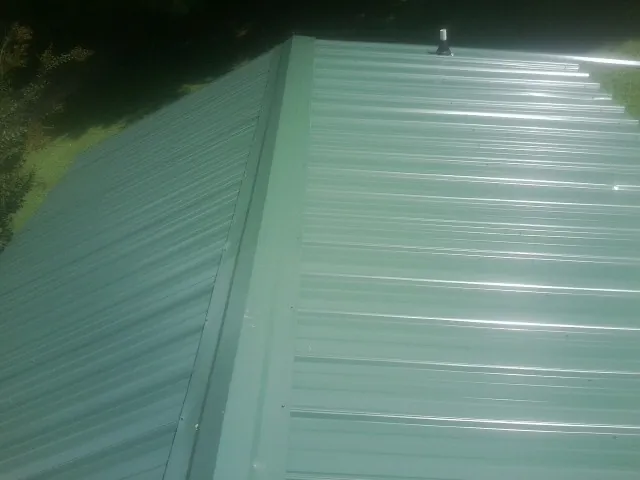 New green metal panels meeting at the ridge of a roof — Flat Roof Repair work by our crew in Flower Mound