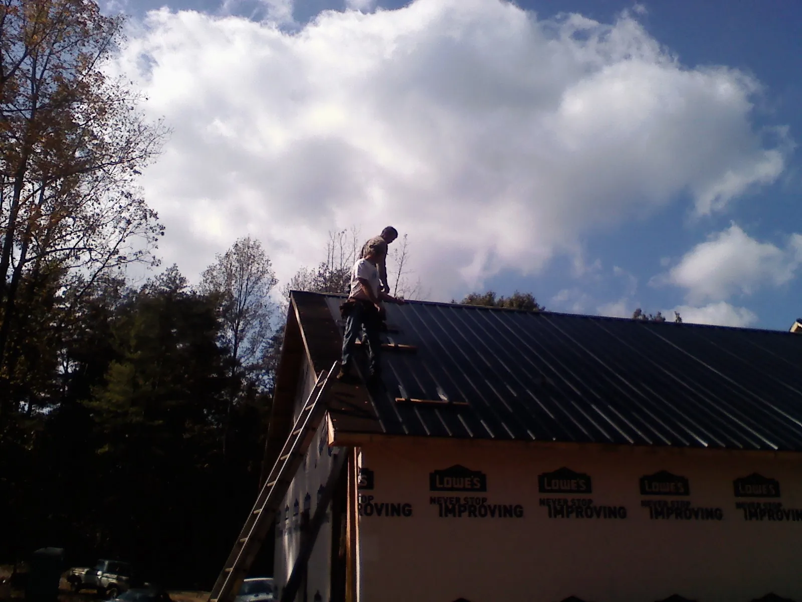 Roofer fastening dark metal panels high against a cloudy sky, from a Roof Inspection job in Flower Mound