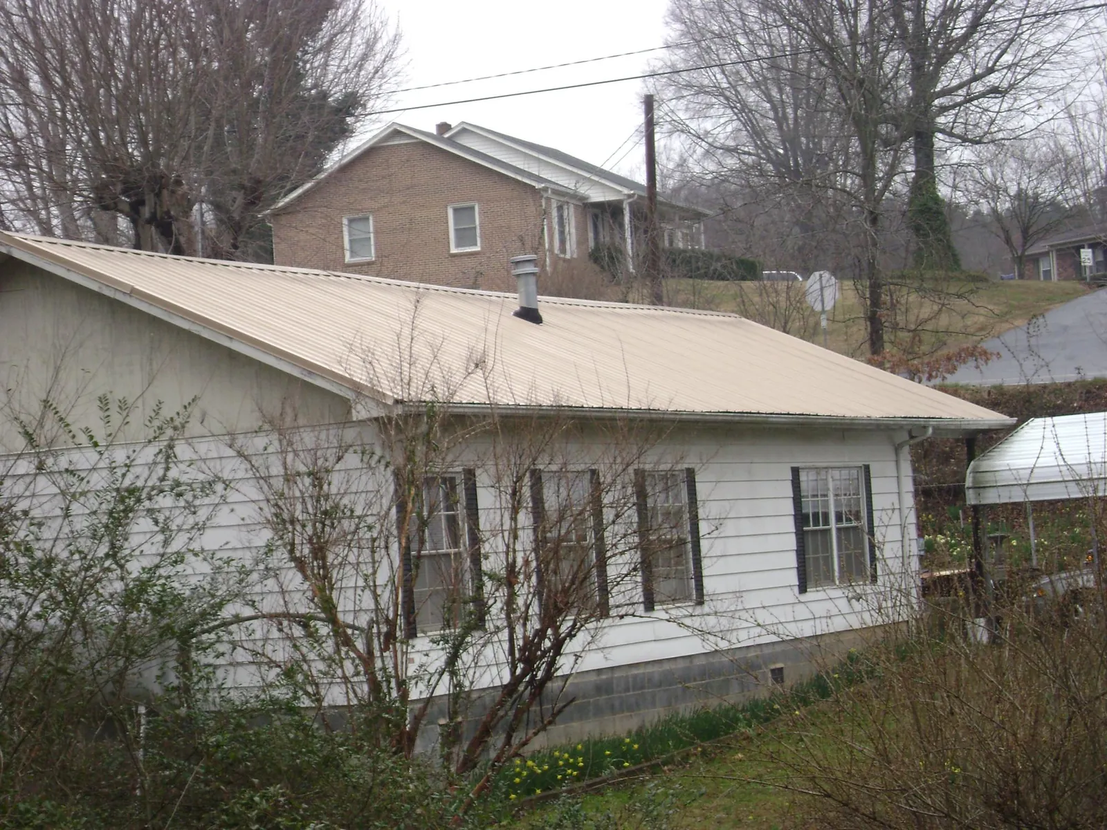 Tan metal roof on a white sided house set into a hillside — Commercial Roofing by Roofing Brothers in Flower Mound